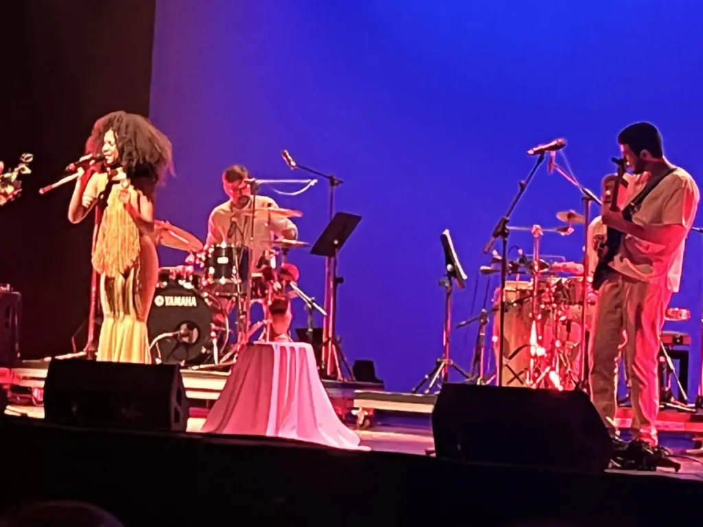 Guitarrista y batería de Kairos Music en concierto, con pantalla azul de fondo