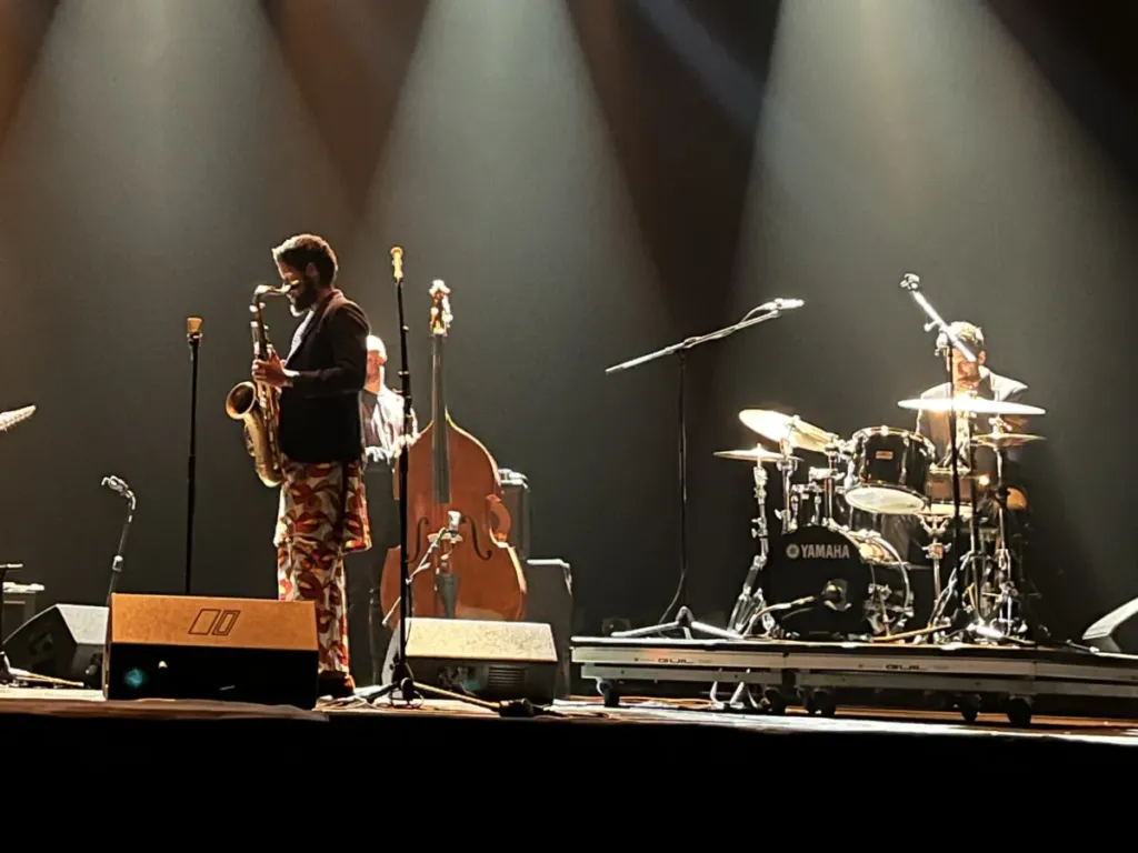 Saxofonista, contrabajista y batería de Kairos Music en directo, con haces de luz sobre el escenario